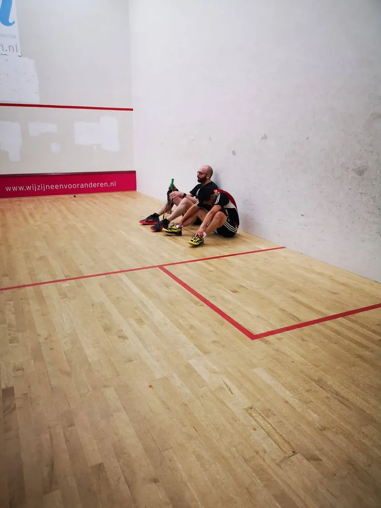 Two players sitting against the back wall of a squash court, catching their breath after a match