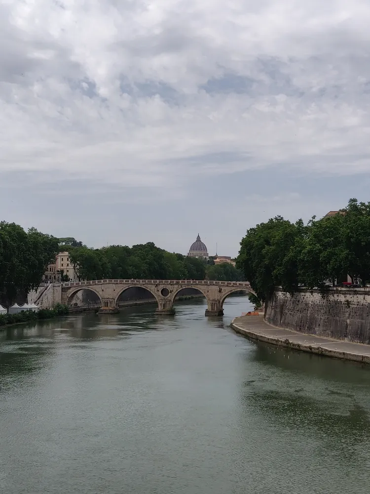 The Tiber in Rome, a stone arch bridge crossing it and the dome of St Peter's beyond